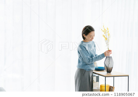 A woman in her 30s decorating her room with flowers A woman in her 30s decorating her room with flowers 118905067