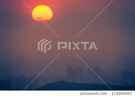 Silhouette of an Airplane Flying Past the Setting Sun Over Taipei City. 118906065