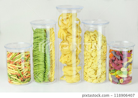 Varieties of multi-colored pasta in glass containers. Types of uncooked pasta. Pattern of gastronomy. Storing different types of pasta at home. 118906407