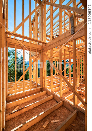 Under-construction residential wooden frame home located near a forest. Commencement of a new construction project for a cozy house or a mountain cottage. Idea of contemporary ecological construction. 118906541