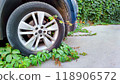 Creeping green plants overtake car tire, embodying nature resilience in urban spaces, contrast with mechanical progress, concept of environmental balance. 118906572