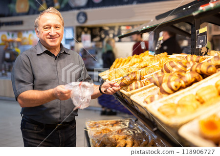 Man takes muffins on shelf of bakery section 118906727