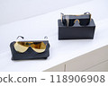 Two pairs of stylish sunglasses with gold and black lenses displayed on sleek black cases, modern minimalistic design, fashion-forward accessories, luxury eyewear, retail presentation, premium look. 118906908
