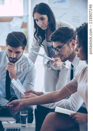 Take a look at this numbers! Young beautiful African woman pointing at her laptop while sitting on the couch at office with her coworkers Take a look at this numbers! Young beautiful African woman pointing at her laptop while sitting on the couch at office with her coworkers 118907246