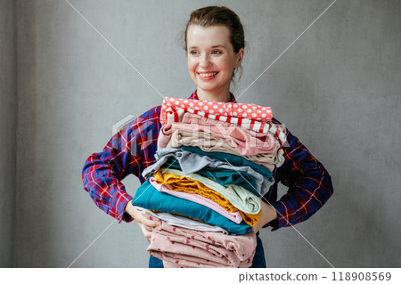 happy young European woman holds stack of folded clothes for hygienic washing at home. happy young European woman holds stack of folded clothes for hygienic washing at home. 118908569