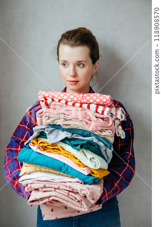 happy young European woman holds stack of folded clothes for hygienic washing at home.  118908570