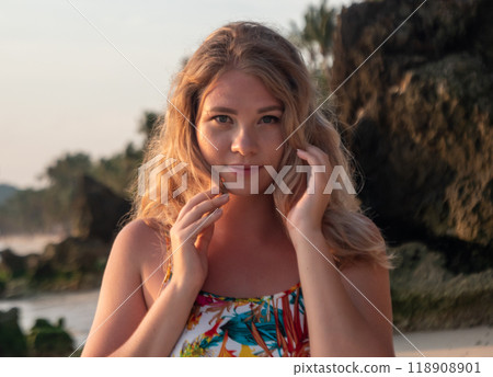 Portrait of a young woman with wavy blonde hair stands at the beach at the sunset. Portrait of a young woman with wavy blonde hair stands at the beach at the sunset. 118908901