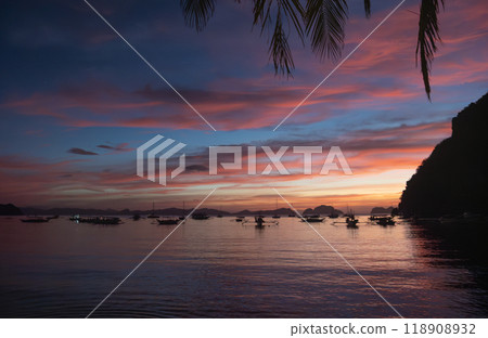 Sunset view over calm waters with boats anchored near the shoreline in a tropical location. El NIdo, Palawan. Sunset view over calm waters with boats anchored near the shoreline in a tropical location. El NIdo, Palawan. 118908932