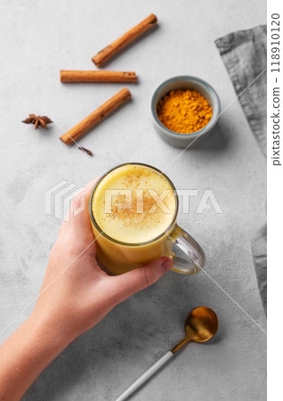 Hand holding turmeric golden milk latte with spices and honey. Detox, immunity boosting drink 118910120