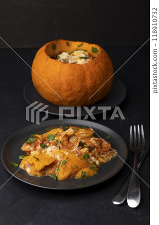Whole baked pumpkin with tiger prawns, melted cheese and tomatoes. Traditional dish of Brazil, home cooking. Selective focus, close-up, black background. Whole baked pumpkin with tiger prawns, melted cheese and tomatoes. Traditional dish of Brazil, home cooking. Selective focus, close-up, black background. 118910732