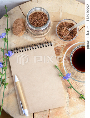 Notepad, pen, chicory flowers, granular powder, chicory tea on wooden stump. Copy space. Top view. 118910992