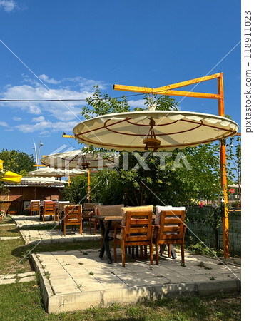 Outdoor seating area with large canvas umbrellas and wooden furniture under a clear blue sky in hotel resort creates an inviting and relaxed atmosphere. Setting is perfect for enjoying sunny days in a Outdoor seating area with large canvas umbrellas and wooden furniture under a clear blue sky in hotel resort creates an inviting and relaxed atmosphere. Setting is perfect for enjoying sunny days in a 118911023