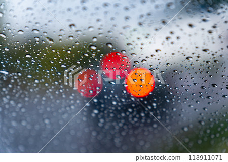 Raindrops create a textured effect on the car window, blurring bright red lights from vehicles ahead in the busy city as rain falls steadily Raindrops create a textured effect on the car window, blurring bright red lights from vehicles ahead in the busy city as rain falls steadily 118911071