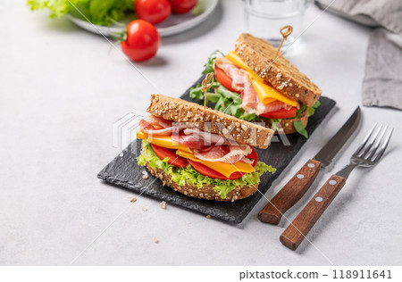 Two toast club sandwiches made of grain bread with cheddar cheese and bacon stuffed with tomatoes  118911641