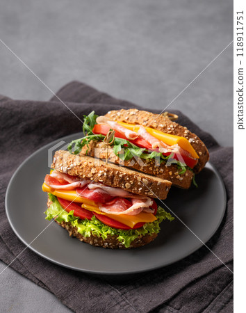 Club sandwich on a plate with a bacon, cheese, tomato and lettuce on a dark background. Club sandwich on a plate with a bacon, cheese, tomato and lettuce on a dark background. 118911751