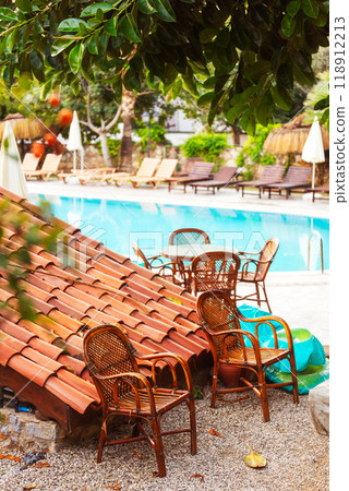 Two empty rotary stools under a tree near the pool and a tiled roof 118912213