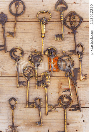 A collection of old and rusted keys are hanging on a wooden wall 118912230