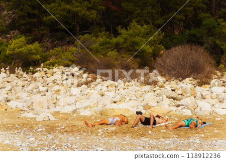 people laying on a rocky beach with trees in the background 118912236