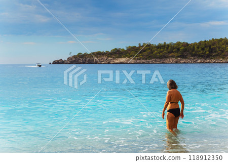 A woman wearing a bikini is happily walking into the ocean waves A woman wearing a bikini is happily walking into the ocean waves 118912350