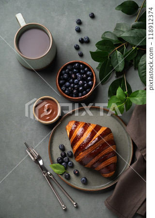 Flat lay of fresh croissant with chocolate and blueberries on a dark plate on a green background  118912374