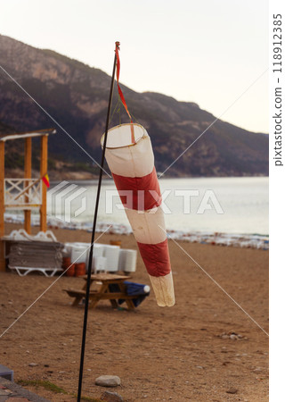 A colorful red and white wind vane is hanging from a tall pole on the beach 118912385