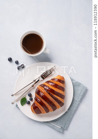 Fresh croissant with chocolate and blueberries on a white plate on a light background Fresh croissant with chocolate and blueberries on a white plate on a light background 118912390