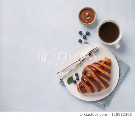 Fresh croissant with chocolate and blueberries on a white plate on a light background Fresh croissant with chocolate and blueberries on a white plate on a light background 118912398