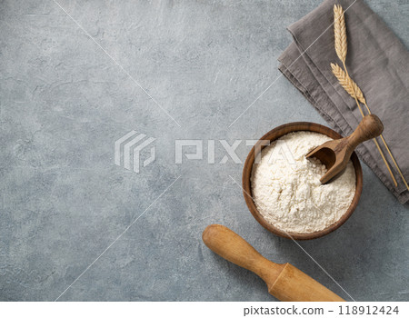 Wheat flour in a wooden bowl with a scoop and rolling pin on a blue background.  118912424