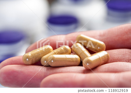 Hand holds natural capsules filled with herbal ingredients and extracts, surrounded by pharmaceutical containers. Alternative medicine supplements concept Hand holds natural capsules filled with herbal ingredients and extracts, surrounded by pharmaceutical containers. Alternative medicine supplements concept 118912919