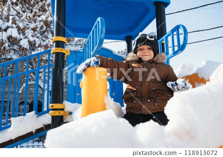 A Caucasian child is having fun riding down a slide in winter. 118913072