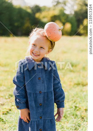 Autumn harvest organic pumpkins and apples. Happy little toddler girl on pumpkin patch on cold autumn day, with lot of pumpkins for Halloween or thanksgiving and red wagon. Children on pumpkin field. 118913164