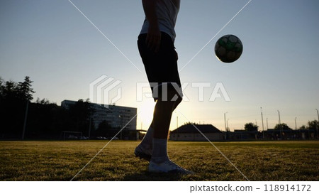 Legs of young man kicking ball at green field. Male feet of professional footballer juggling soccer ball on stadium at sunset. Sportsman practicing tricks outdoor. Concept of a freestyle football Legs of young man kicking ball at green field. Male feet of professional footballer juggling soccer ball on stadium at sunset. Sportsman practicing tricks outdoor. Concept of a freestyle football 118914172