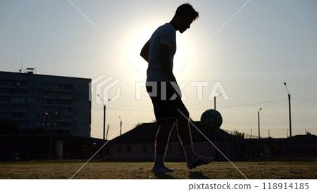Professional footballer juggling soccer ball on stadium at sunset. Young man kicking ball at green field. Sportsman practicing tricks at meadow with sunlight at background. Freestyle football concept Professional footballer juggling soccer ball on stadium at sunset. Young man kicking ball at green field. Sportsman practicing tricks at meadow with sunlight at background. Freestyle football concept 118914185