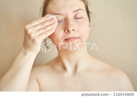 Woman cleansing face with cotton pad for natural skincare routine at home 118914809