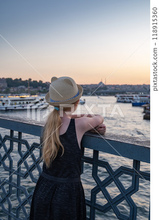A girl in a hat on the bridge looks at the mosque and the Bosphorus Strait with ships.  A girl in a hat on the bridge looks at the mosque and the Bosphorus Strait with ships.  118915360