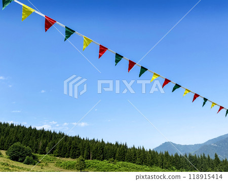 Multicolored garlands or flag flutter in the wind on a summer sunny day on mountain with a blue sky. Multicolored garlands or flag flutter in the wind on a summer sunny day on mountain with a blue sky. 118915414