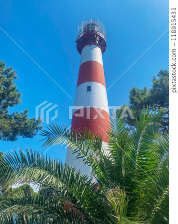 Landscape with a white-red lighthouse in a port city among the palm trees on a summer day. Landscape with a white-red lighthouse in a port city among the palm trees on a summer day. 118915431