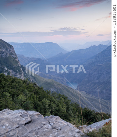 A beautiful landscape of mountains with bushes, rocks and a river on a summer day at sunset.  118915601