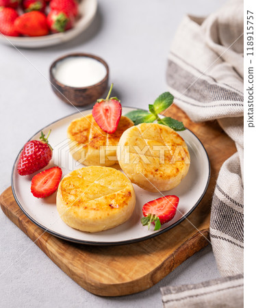Cottage cheese, cheesecakes or syrniki with strawberries and mint leaves on a cutting board Cottage cheese, cheesecakes or syrniki with strawberries and mint leaves on a cutting board 118915757