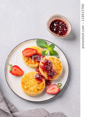 Cottage cheese, cheesecakes or syrniki sprinkled berry sauce on a white plate with strawberry Cottage cheese, cheesecakes or syrniki sprinkled berry sauce on a white plate with strawberry 118915760