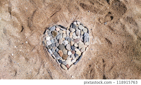 Sea pebbles in the shape of a heart on a sandy beach. Romantic holiday concept or symbol of love. Sea pebbles in the shape of a heart on a sandy beach. Romantic holiday concept or symbol of love. 118915763