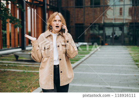 Angry woman on cell phone walking outside building. Frustrated woman talking on phone. Summer time. Negative people emotion Angry woman on cell phone walking outside building. Frustrated woman talking on phone. Summer time. Negative people emotion 118916111