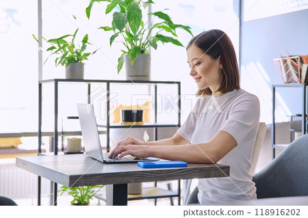 Young woman typing on laptop computer, sitting at table in coworking space, coffee shop 118916202