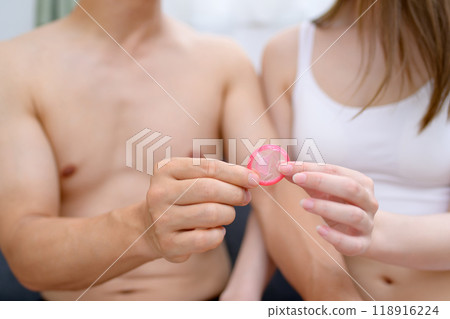 Woman recommending the use of contraception; Young woman's hand holding a condom; Male and female couple holding contraception; Married couple; Pregnancy planning; Sexual consent 118916224