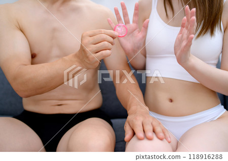 A man encouraging a woman to use contraception and a woman refusing, a man's hand holding a condom, couple, pregnancy, sexual consent, family planning A man encouraging a woman to use contraception and a woman refusing, a man's hand holding a condom, couple, pregnancy, sexual consent, family planning 118916288