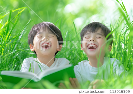 Two children joyfully reading a book together in a lush green field during a sunny day Two children joyfully reading a book together in a lush green field during a sunny day 118916509