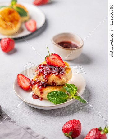 Cottage cheese, cheesecakes or syrniki sprinkled berry sauce on a white plate with strawberry Cottage cheese, cheesecakes or syrniki sprinkled berry sauce on a white plate with strawberry 118916580