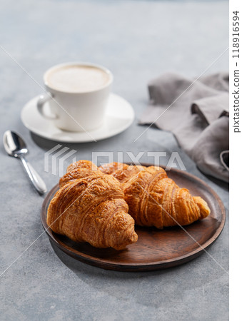 A cup of aromatic cappuccino coffee and fresh croissants in a wooden plate on a blue background A cup of aromatic cappuccino coffee and fresh croissants in a wooden plate on a blue background 118916594