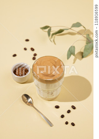 Vegan dalgona coffee. Whipped instant iced coffee with soy milk in a glass on yellow background  118916599