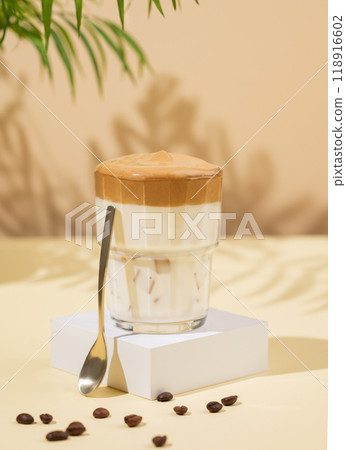 Dalgona coffee. Whipped instant coffee in a glass on a white stand with coffee beans 118916602